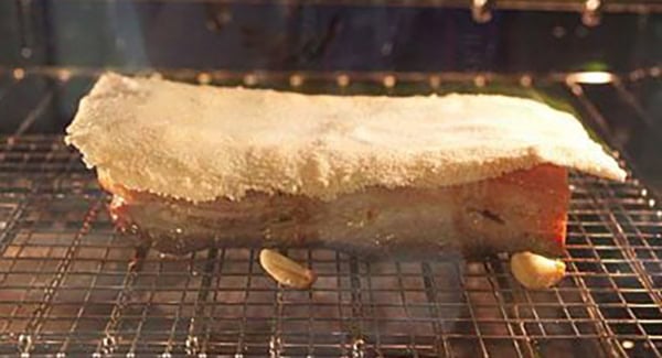 Pork belly with salt crust on a wire rack in an oven. 