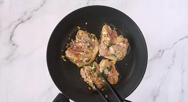 Marinated chicken thighs on a skillet skin-side down. 