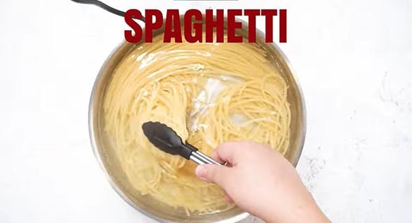 Cooked al dente spaghetti in a pot of hot water, stirred with a tong. 