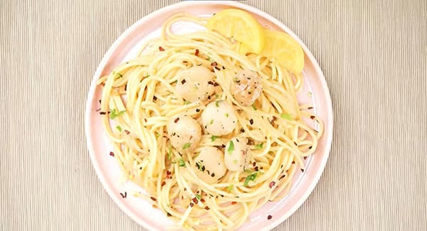 Easy creamy scallop pasta garnished with parsley and served with lemon wedges. 