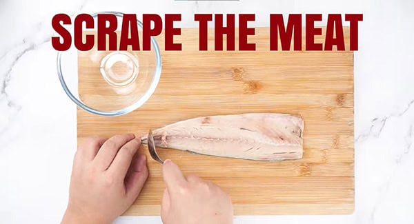 Fish meat being scraped with a metal spoon. 