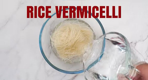 Water is being poured into a bowl with rice vermicelli noodles. 
