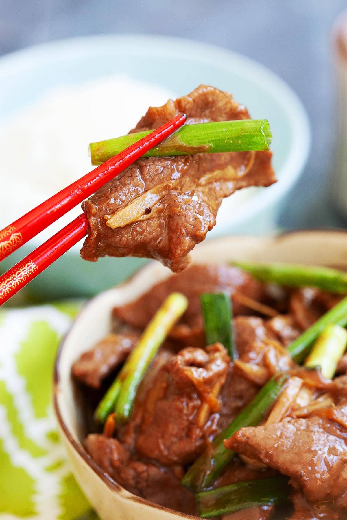 A pair of chopsticks holding tender beef with ginger and scallion. 