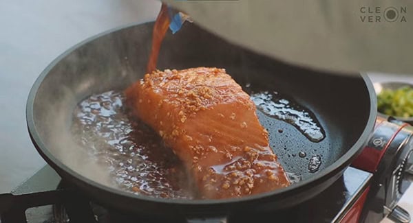 The reserved marinade being poured into the skillet with the salmon fillet. 