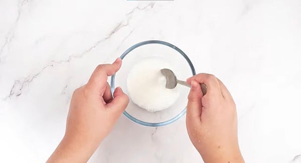Constarch and water being mixed with a spoon in a bowl. 