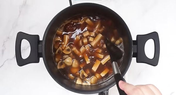 Sauces for hot and sour soup recipe, soft tofu, white button mushrooms and cornstarch mixture in a pot being stirred with a spatula.