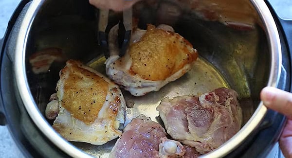 Browned chicken in instant pot being flipped with a tong. 