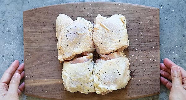 Chicken thighs seasoned in salt and pepper on a chopping board. 