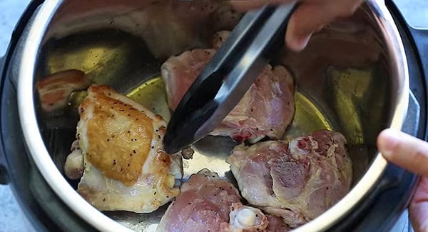 Chicken thighs in instant pot being flipped with a tong. 