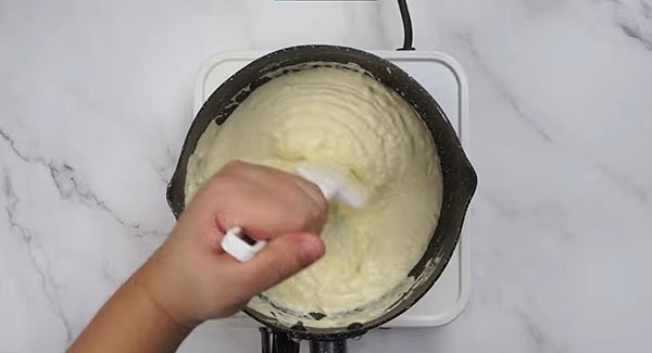 Cream cheese, butter and full milk being melted and mixed together with a spatula in a sauce pan. 