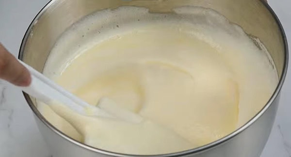 Cream cheese mixture and meringue in a bowl are gently folded using a spatula.