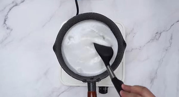 Coconut milk, salt and sugar in a sauce pan being stirred with a spatula. 