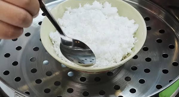 Grated coconut and salt being mixed with a spoon in small bowl which is placed in a steamer. 