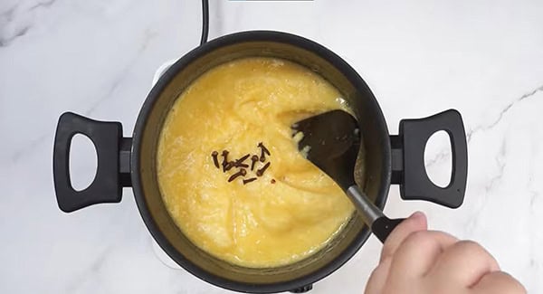 Blended pineapple and cloves in a pot being mixed with a spatula. 