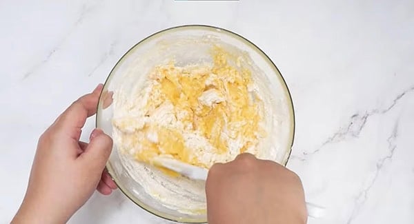 Pineapple cookie dough ingredients in a bowl being mixed with a spatula. 