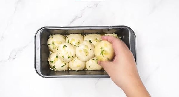 Dough balls dipped in butter mixture is placed into a loaf pan. 