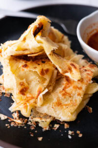 Flaky roti canai on a black serving plate.