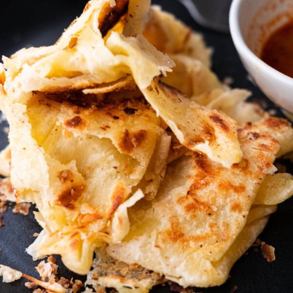 Flaky roti canai on a black serving plate.