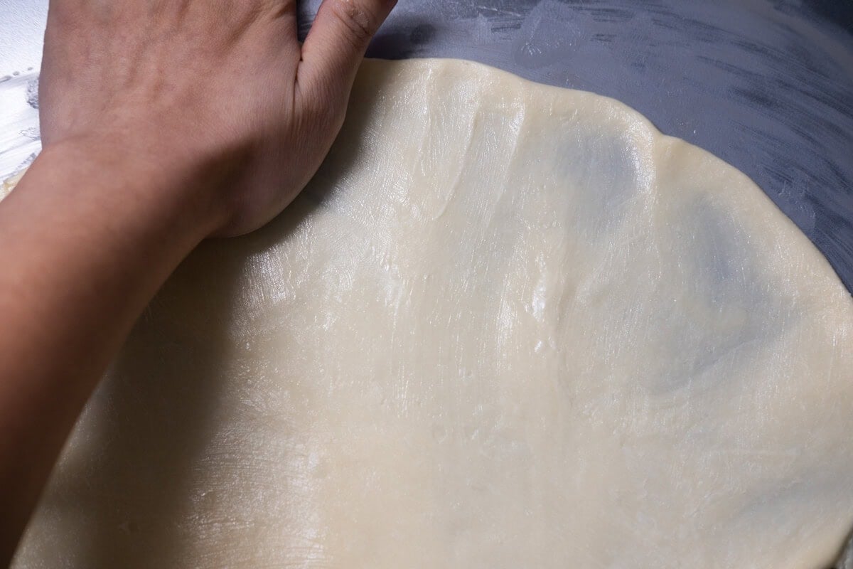 Press with your buttered palm to flatten the dough into a 6-inch (15cm) disc, less than 1/4 inch (5mm) thick, slightly thinner around the edges.