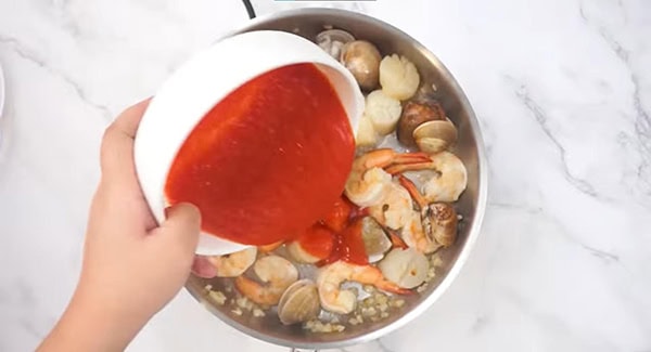 Tomato sauce added into a skillet with shrimp, manila clams, scallop and garlic. 