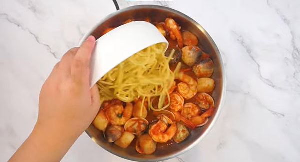 Spaghetti added into a skillet with seafood and tomato sauce. 