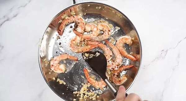 Shrimp, red pepper flakes and garlic in a skillet being stirred with a spatula. 
