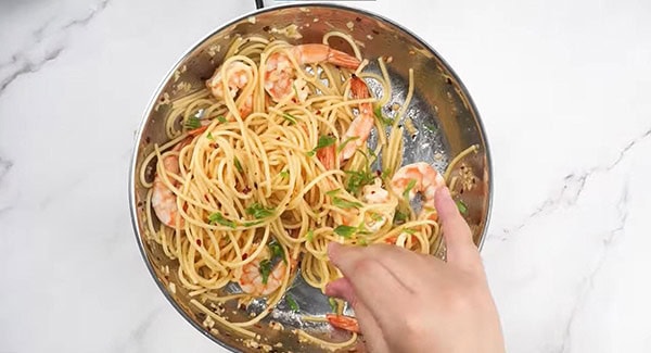 Shrimp spaghetti aglio e olio in a skillet being garnished with parsley. 