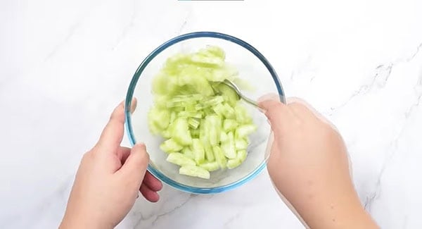 Cucumber and salt in a bowl being mixed with a spoon. 