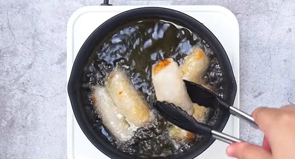Vietnamese spring rolls being fried in oil in a large frying pan. 