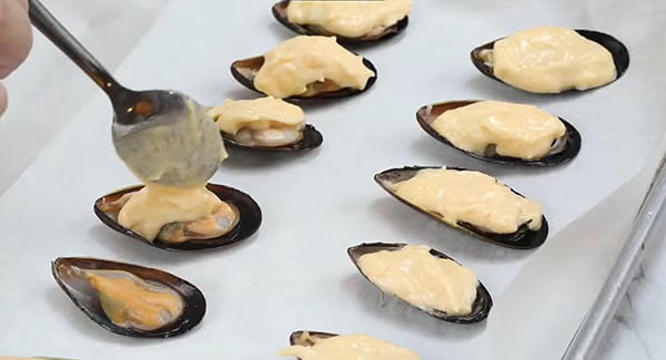 Cheese-mayo mixture being added on top of the mussels. 