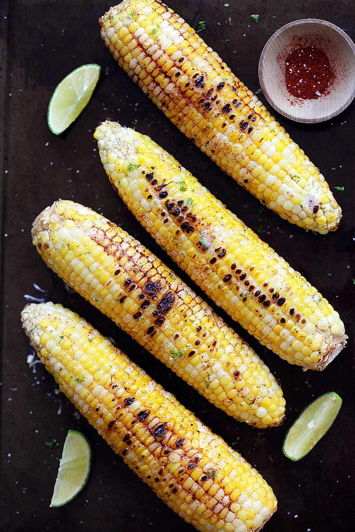 Char grilled corn on the cob with chili lime butter served with lemon wedges and chili seasoning. 