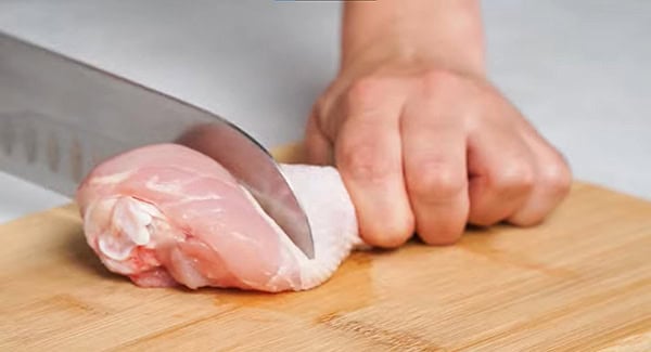 Drumstick being chopped into half on a chopping board. 