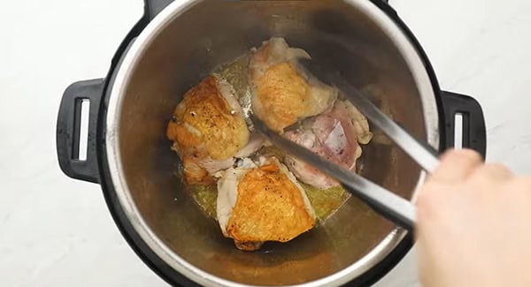 Browned seasoned chicken thighs in an instant pot being flipped with a pair of tongs. 