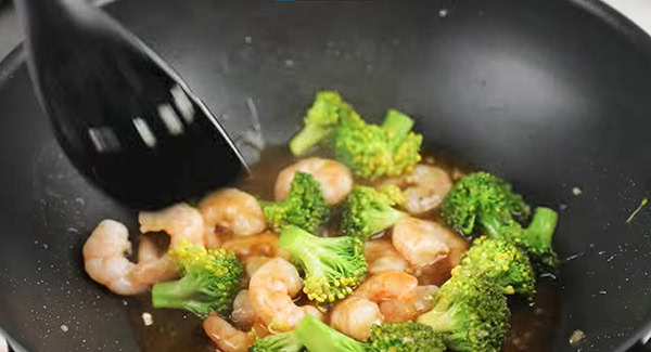 Shrimp and broccoli being stir fried in the sauce. 