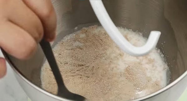 Milk, yeast and sugar in a stand mixer being mixed with a spoon. 