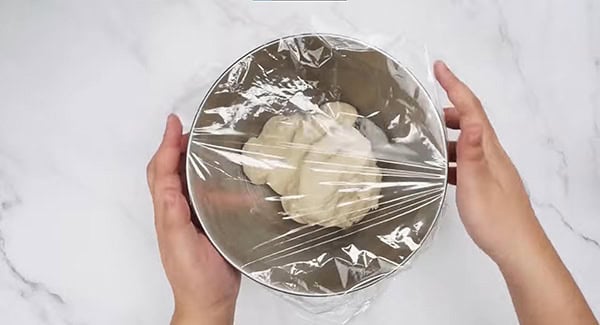 Dough in a bowl covered with plastic wrap. 