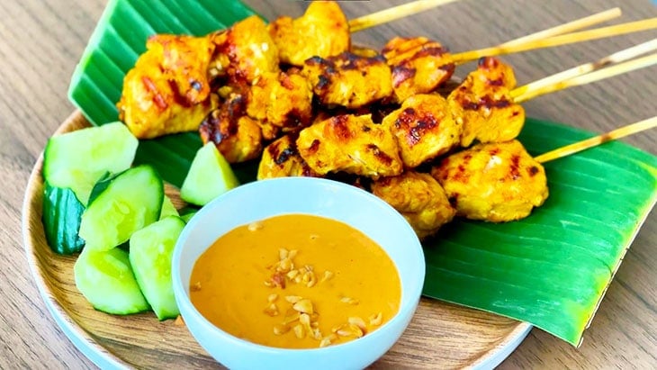 Delicious Thai Chicken Sate served on a plate with cucumber and Thai Peanut Sauce.