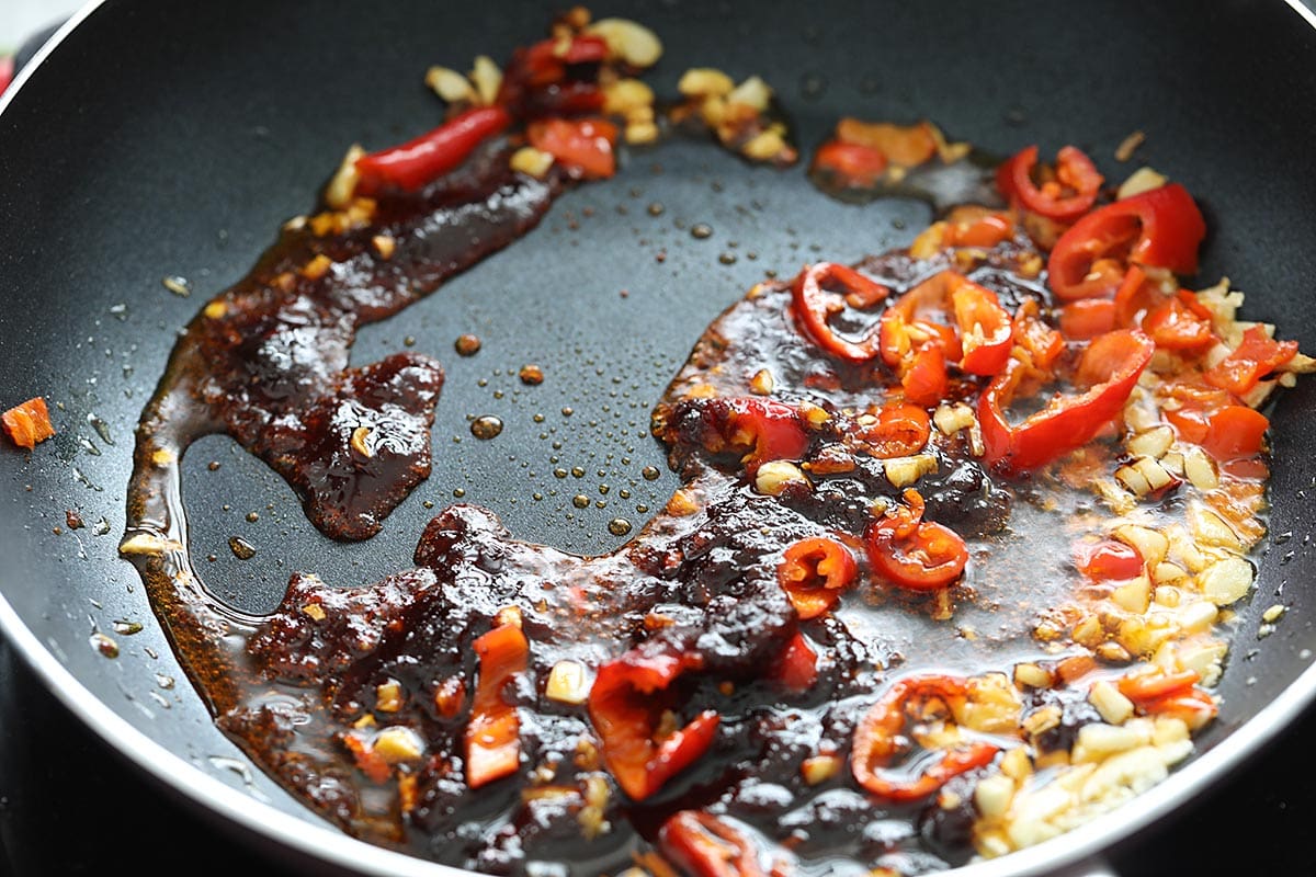 Garlic, nam prik pao and bird's eye chilies in a skillet. 