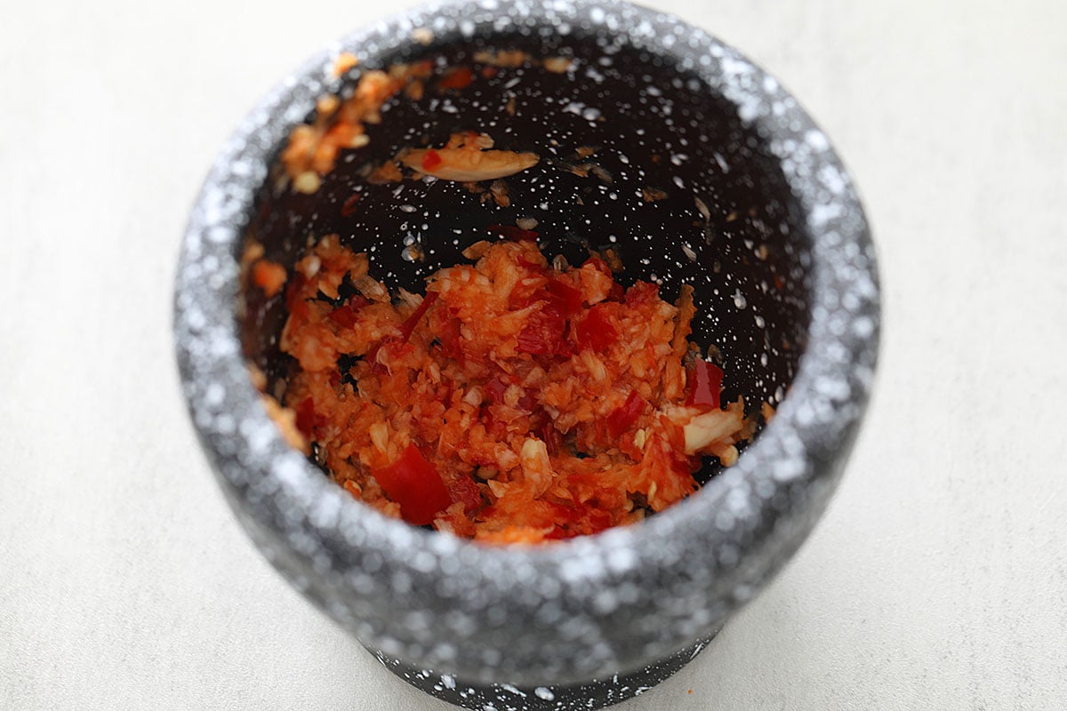 Pounding garlic and Thai chilies in a mortar and pestle.