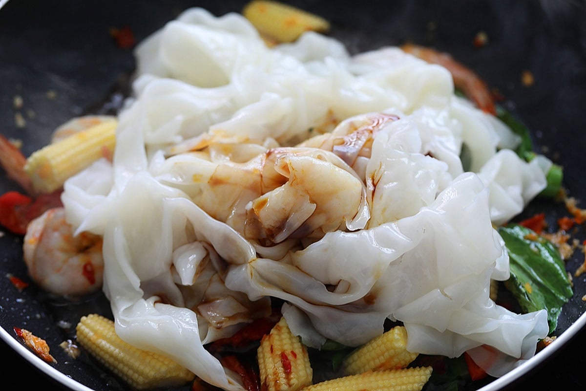 Adding drunken noodles sauce to rice noodles in a skillet. 
