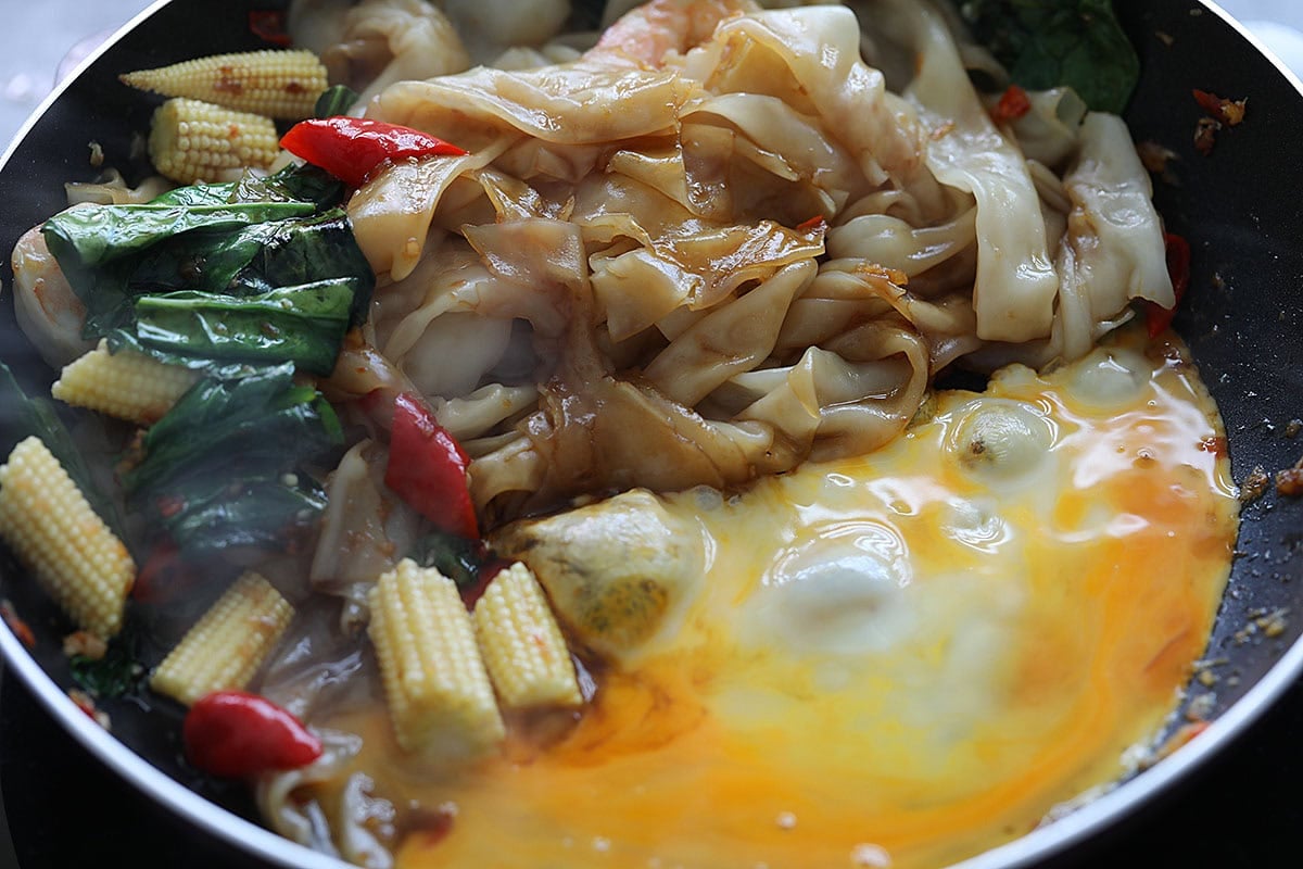 Adding a beaten egg to Pad Kee Mao in a skillet. 