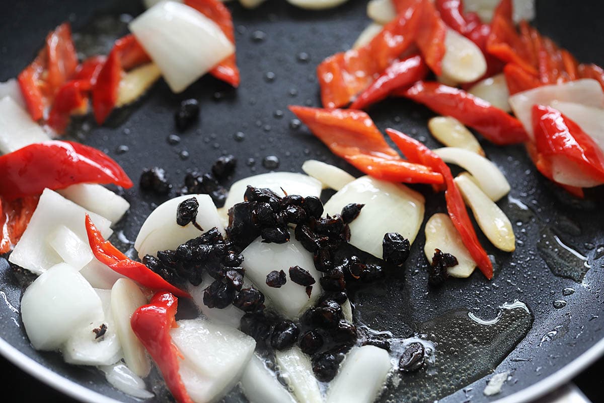 Stir frying aromatics and fermented black beans in a skillet. 