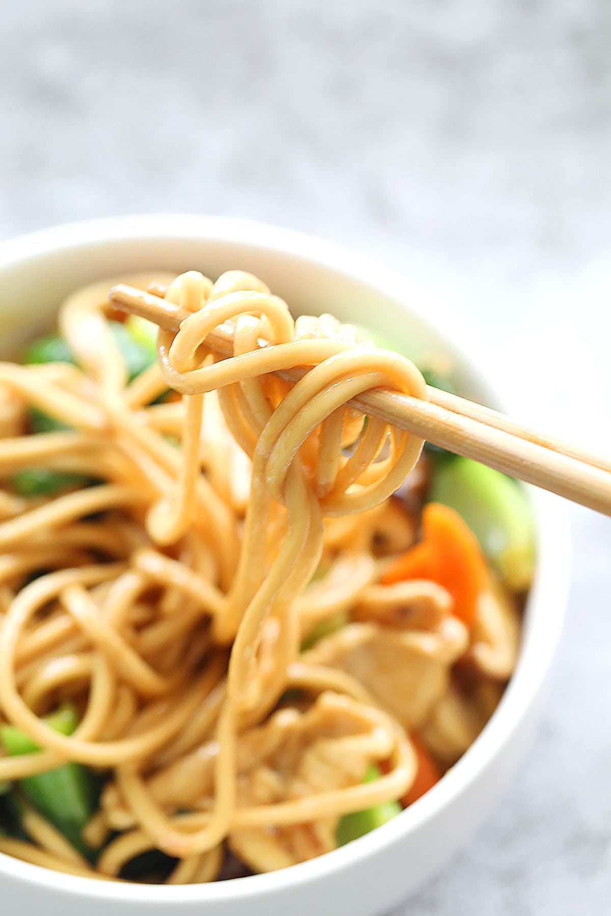 Lo mein noodle strands on a pair of chopsticks.