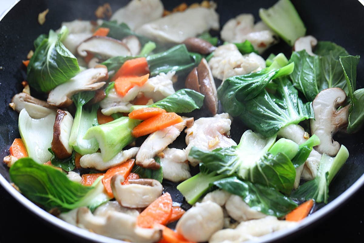 Cooking chicken lo mein with vegetables in a skillet.