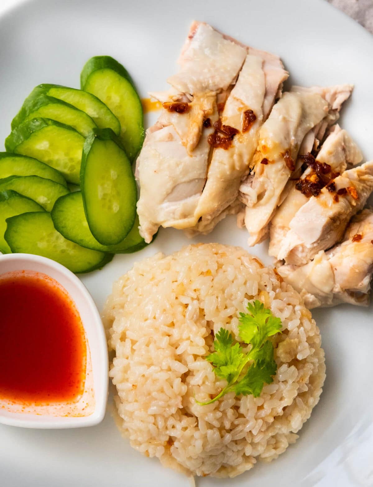 Chicken rice served on a plate with chicken, cucumber and chili sauce. 