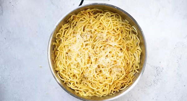 Garlic noodles topped with grated parmesan cheese in a skillet.