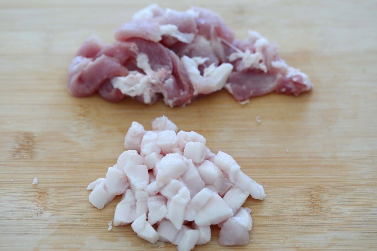 Diced pork fat and pork meat slices on a cutting board.