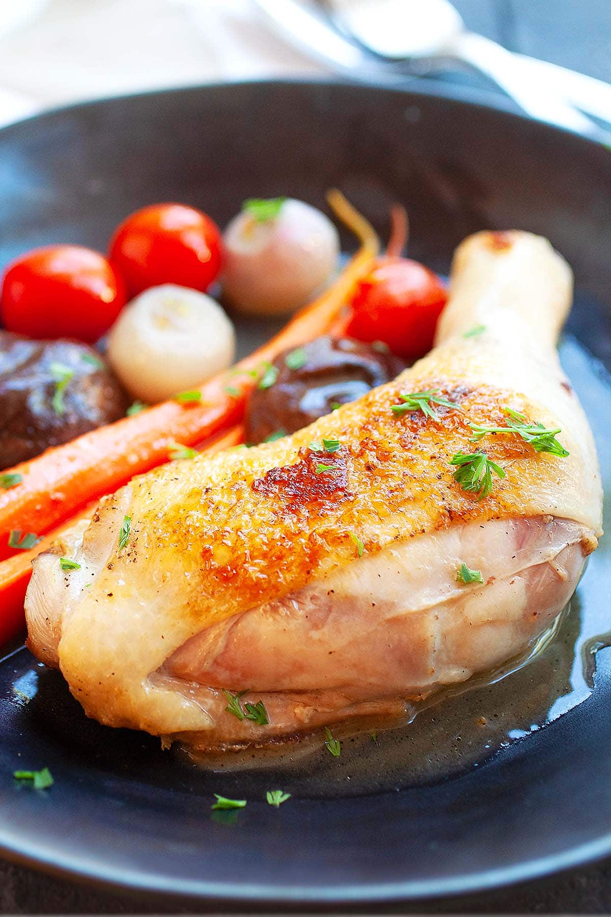 Tender and juicy braised chicken thigh on a black plate.