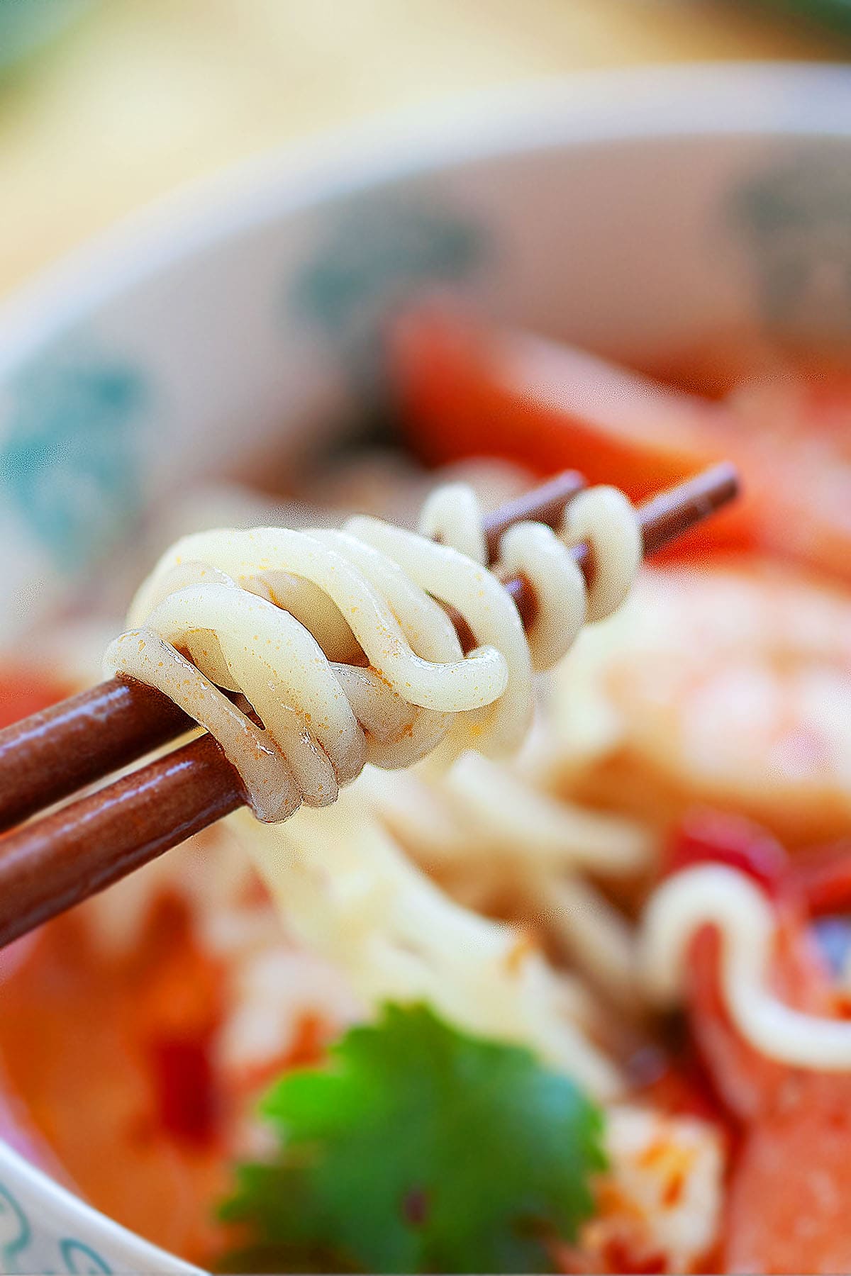 Strands of tom yum ramen picked up by a pair of chopsticks.