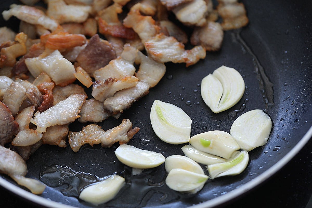 Slightly browned pork belly slices and garlic in a wok.